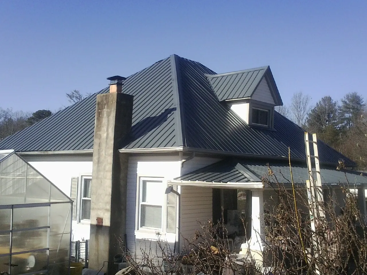 Dark blue standing seam metal roof on a white farmhouse with dormer — Slate & Tile Roof Repair by Roofing Brothers in Huntingtown