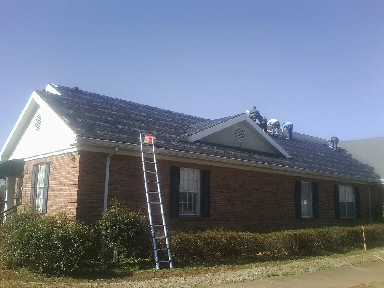 Crew tearing shingles off a brick ranch roof with a ladder set — Metal Roof Repair work by our crew in Huntingtown