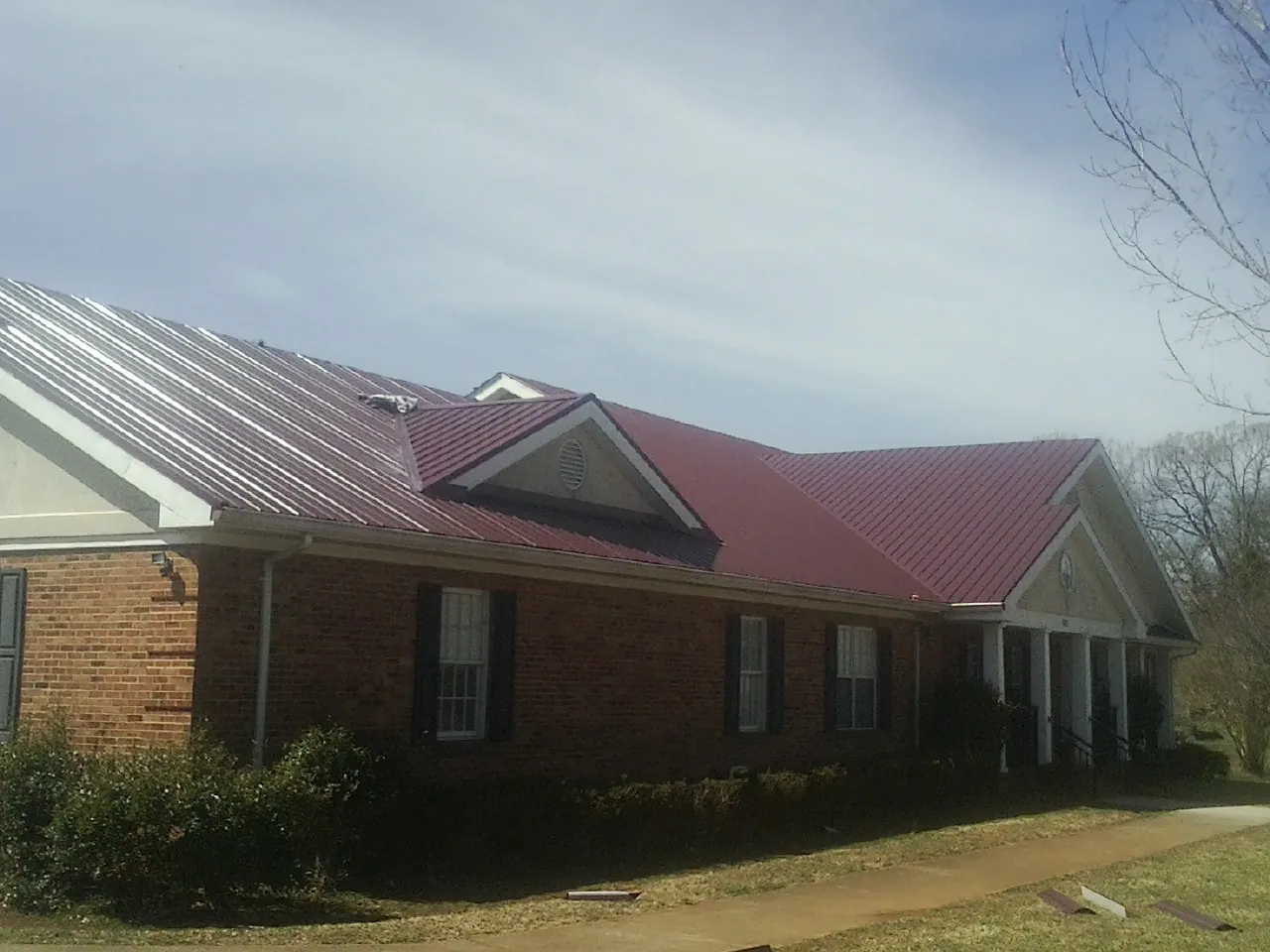 Red metal roof with gabled entries on a long brick building, from a Hail Damage Roof Repair job in Huntingtown