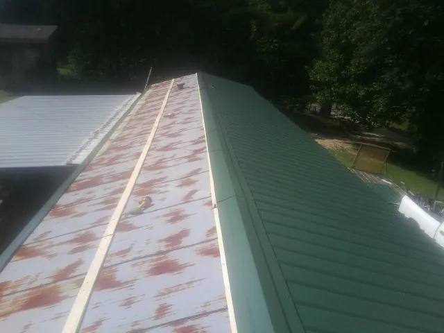 Old rusted panels beside newly installed green metal roofing — Wind Damage Roof Repair by Roofing Brothers in Huntingtown
