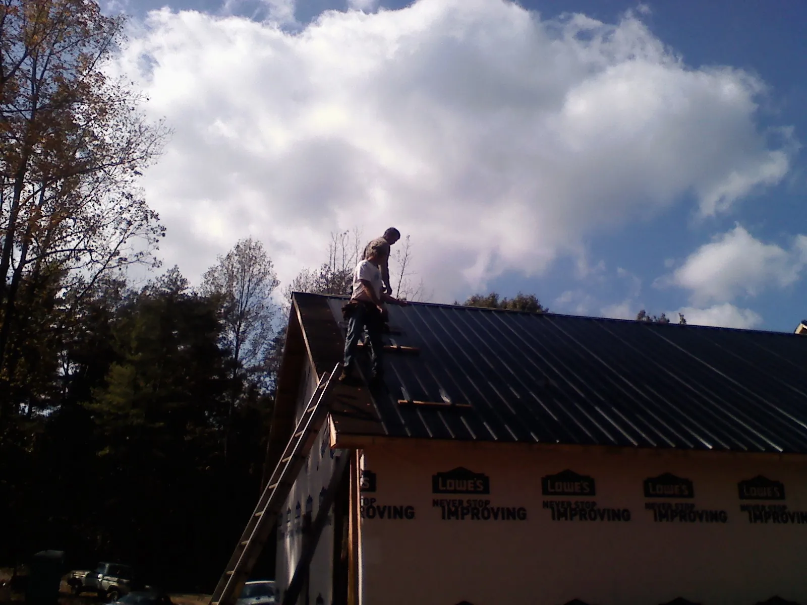 Roofer fastening dark metal panels high against a cloudy sky, from a Roof Inspection job in Huntingtown