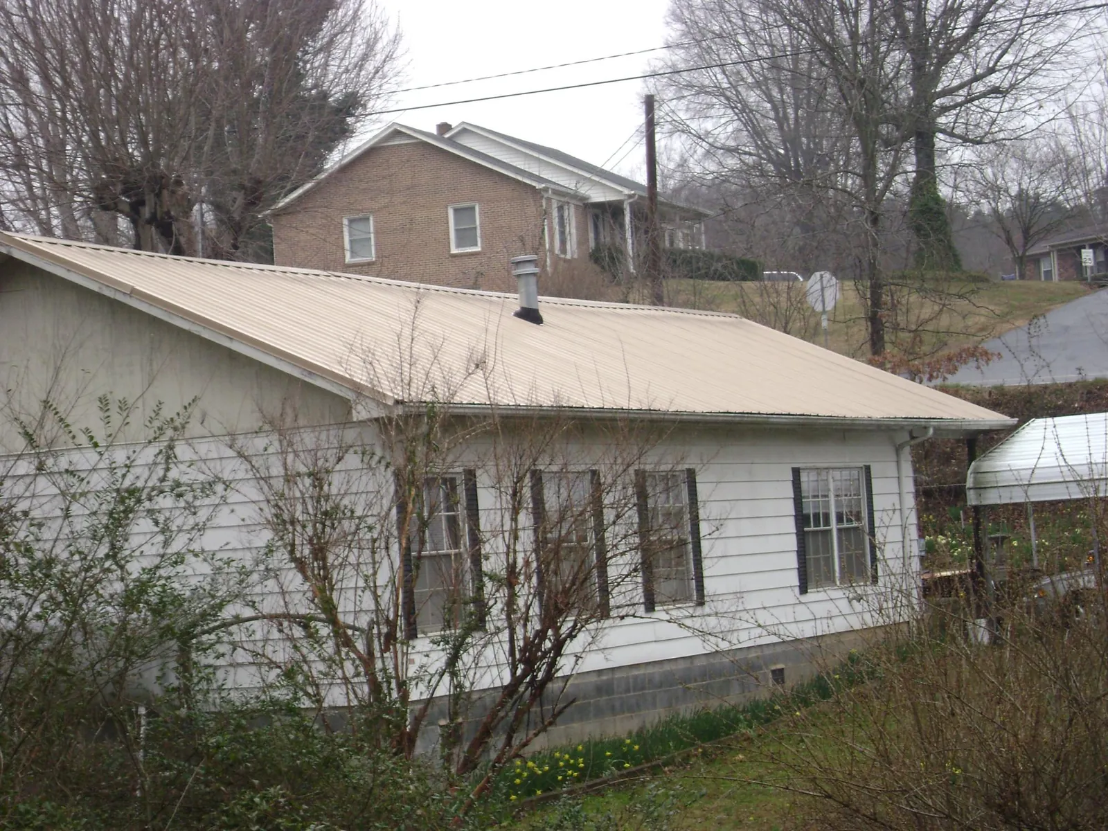 Tan metal roof on a white sided house set into a hillside — Commercial Roofing by Roofing Brothers in Huntingtown